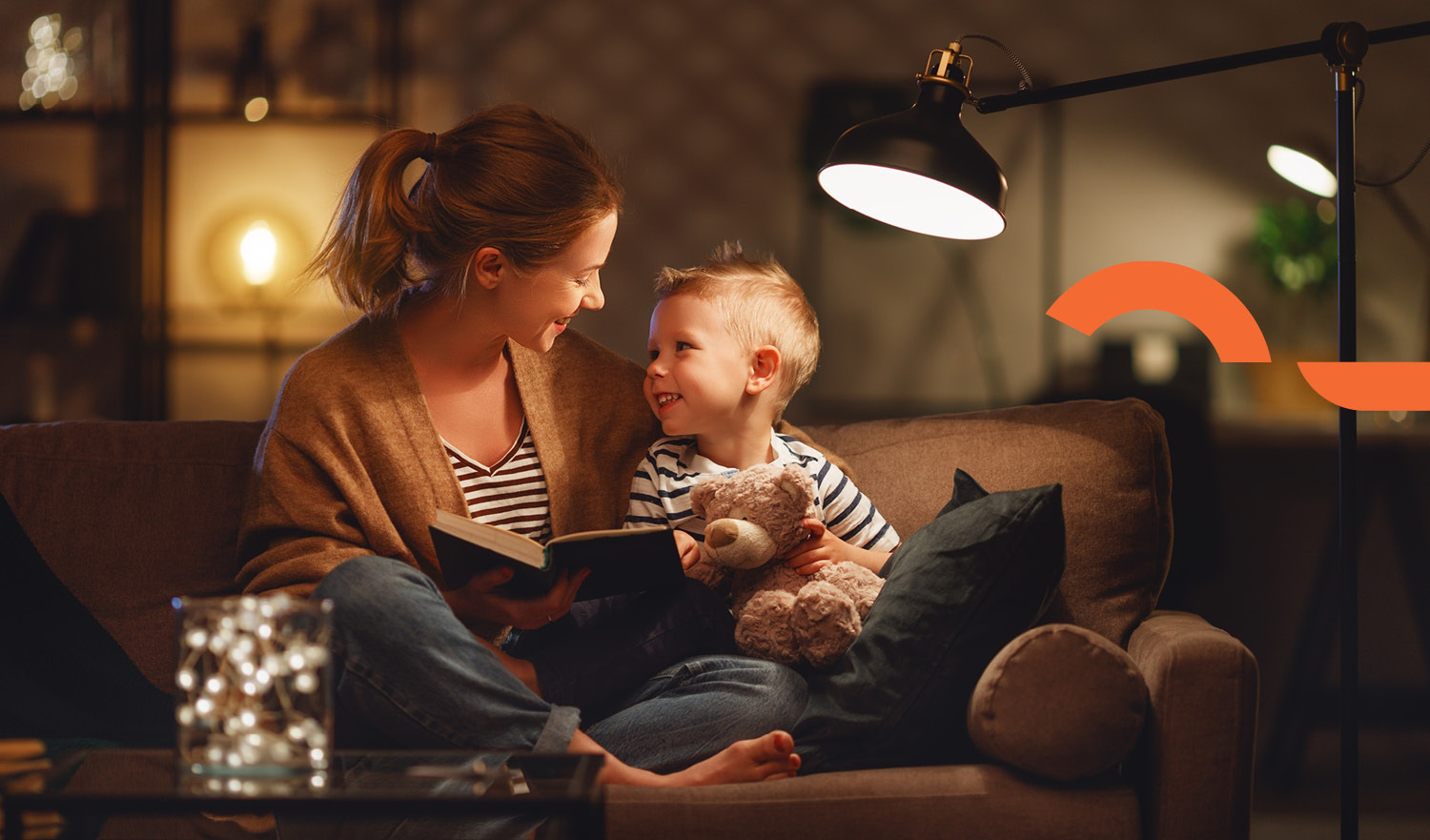 Mother and young boy reading a book on couch with cosy dim light